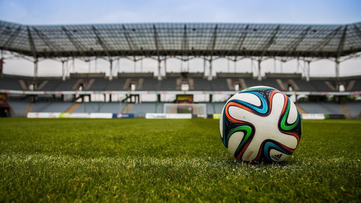 Uma bola de futebol em campo com um estádio vazio ao fundo
