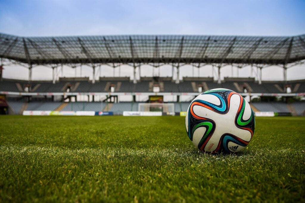 Uma bola de futebol colorida em um campo verde com um estádio ao fundo.