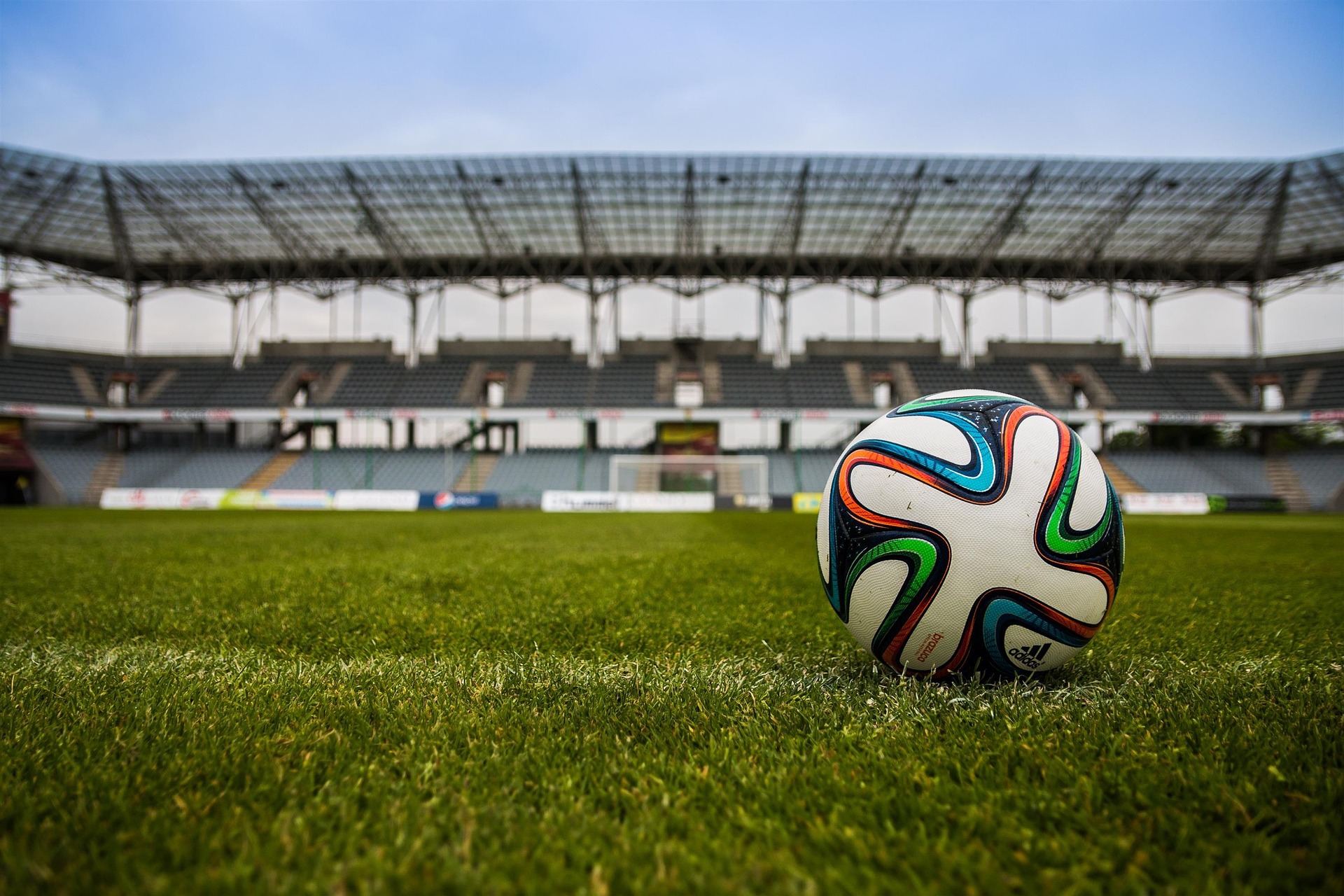 Uma bola de futebol colorida em um campo verde com um estádio ao fundo.